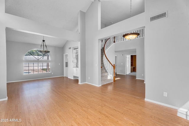 interior space featuring visible vents, stairs, wood finished floors, baseboards, and high vaulted ceiling