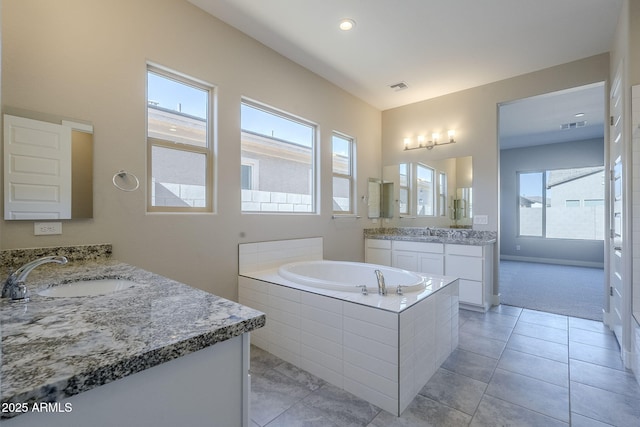 bathroom with tile patterned flooring, a relaxing tiled tub, and vanity