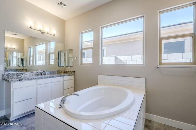 bathroom featuring tile patterned flooring, a relaxing tiled tub, and vanity