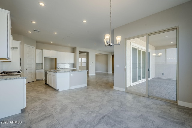 kitchen with pendant lighting, white cabinetry, a center island with sink, and a chandelier