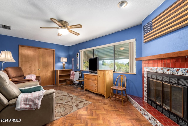 living room with a tiled fireplace, ceiling fan, a textured ceiling, and parquet flooring