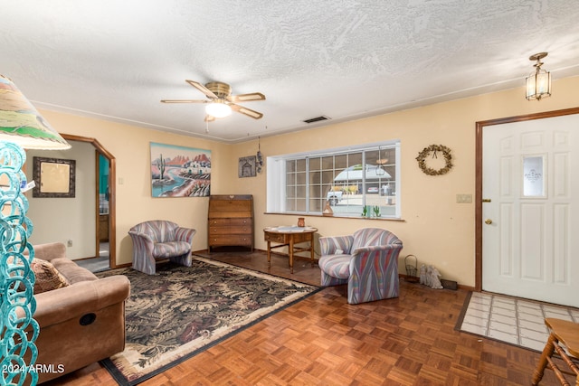 living room with dark parquet flooring, a textured ceiling, and ceiling fan