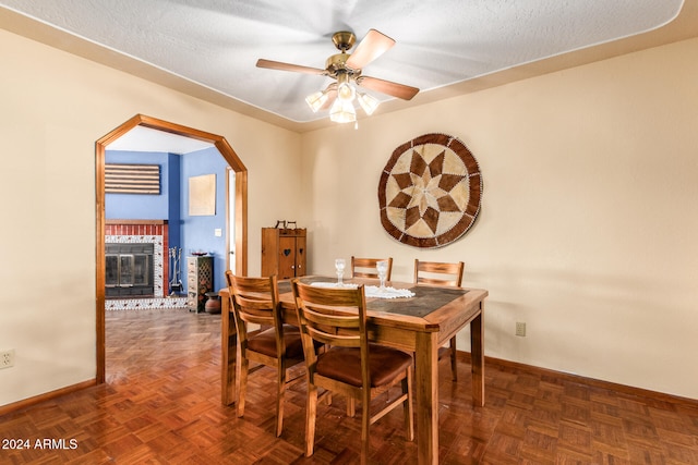 dining area featuring dark parquet flooring, ceiling fan, a fireplace, and a textured ceiling