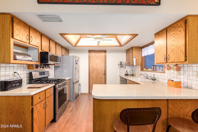 kitchen featuring a skylight, light hardwood / wood-style flooring, tasteful backsplash, kitchen peninsula, and stainless steel appliances