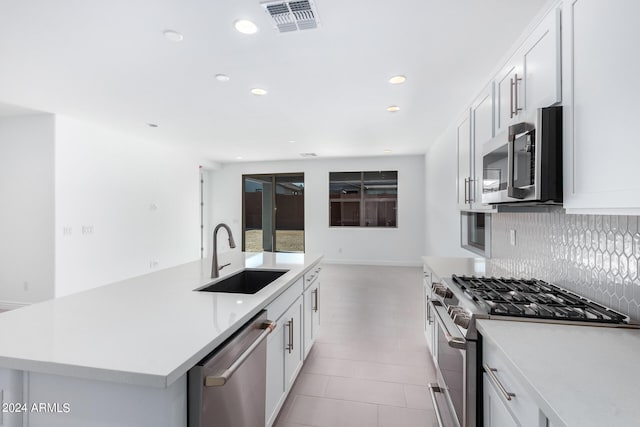 kitchen with sink, backsplash, an island with sink, white cabinets, and appliances with stainless steel finishes