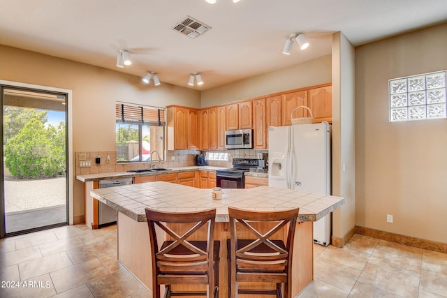 kitchen with decorative backsplash, stainless steel appliances, sink, a center island, and tile counters