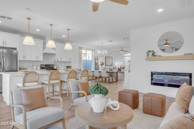 living room with ceiling fan with notable chandelier and light hardwood / wood-style floors