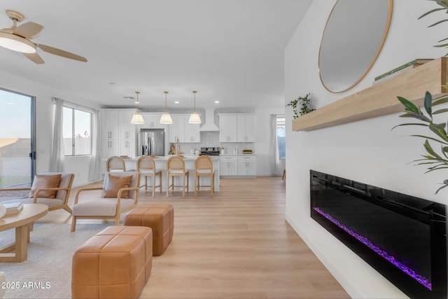 living room featuring sink, a wealth of natural light, ceiling fan, and light wood-type flooring