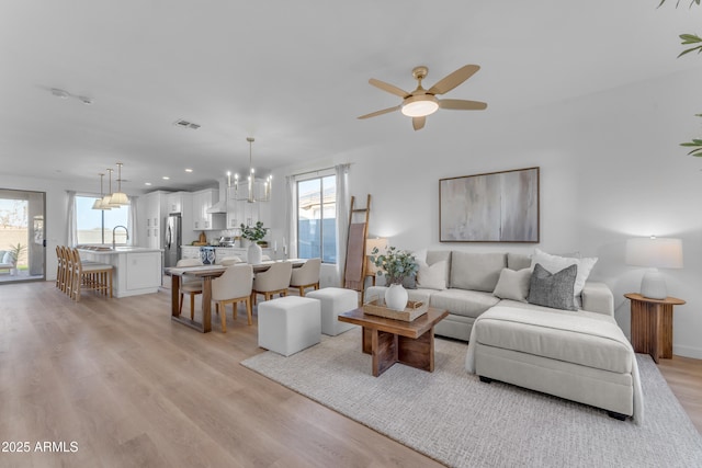 living room with ceiling fan with notable chandelier, a wealth of natural light, sink, and light wood-type flooring