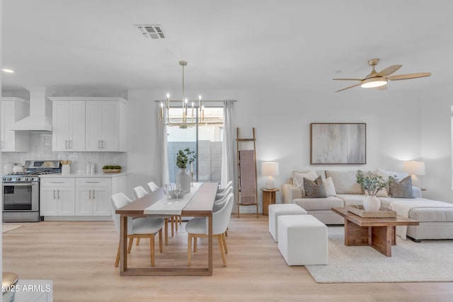 dining area with ceiling fan with notable chandelier and light hardwood / wood-style flooring