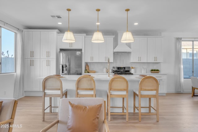 kitchen featuring white cabinetry, appliances with stainless steel finishes, decorative light fixtures, and a center island with sink