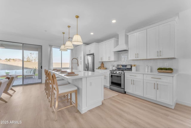 kitchen featuring white cabinetry, hanging light fixtures, stainless steel appliances, and wall chimney exhaust hood