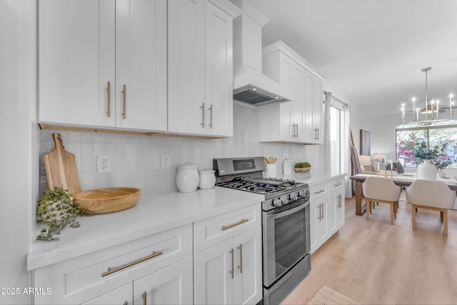 kitchen featuring decorative backsplash, white cabinetry, stainless steel gas range, and wall chimney exhaust hood