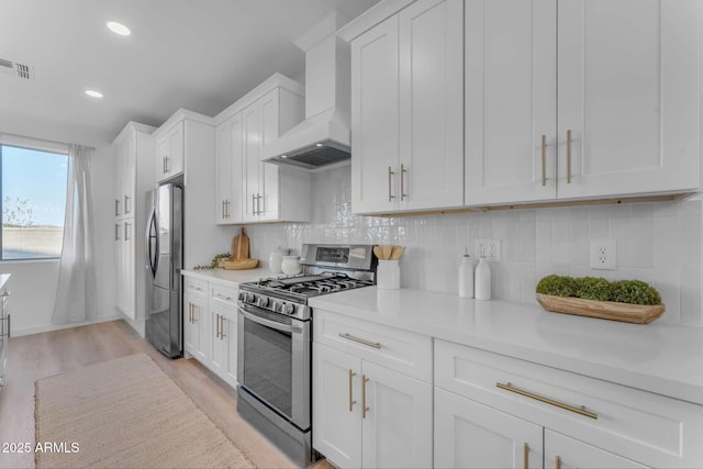 kitchen with stainless steel appliances, light hardwood / wood-style floors, white cabinets, decorative backsplash, and wall chimney exhaust hood