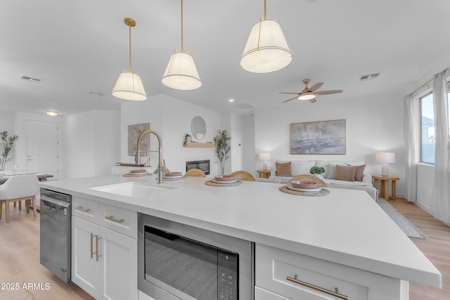 kitchen with built in microwave, sink, a center island with sink, stainless steel dishwasher, and white cabinets