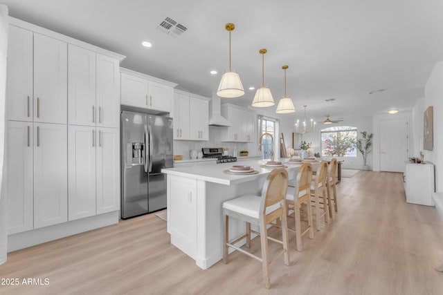 kitchen featuring pendant lighting, white cabinetry, a center island with sink, stainless steel appliances, and a kitchen bar