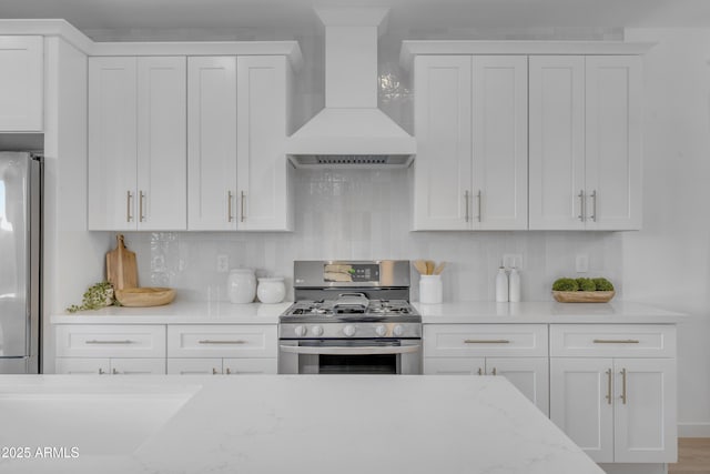 kitchen featuring premium range hood, white cabinetry, stainless steel appliances, light stone counters, and decorative backsplash