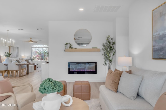 living room featuring ceiling fan with notable chandelier and light hardwood / wood-style flooring