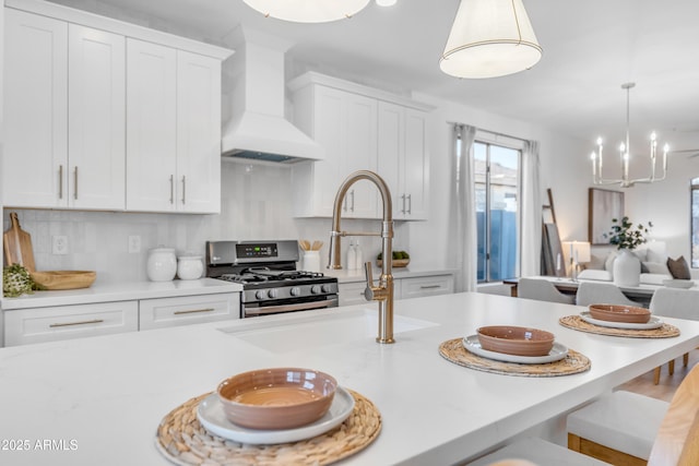 kitchen featuring custom exhaust hood, stainless steel gas stove, white cabinetry, hanging light fixtures, and decorative backsplash