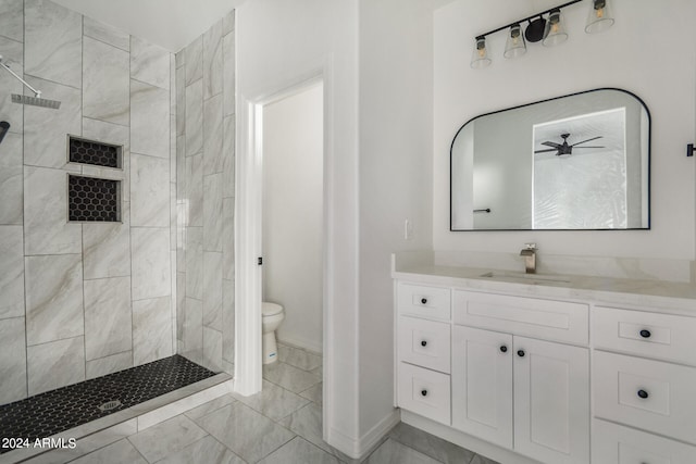 bathroom featuring ceiling fan, tiled shower, toilet, vanity, and tile patterned flooring