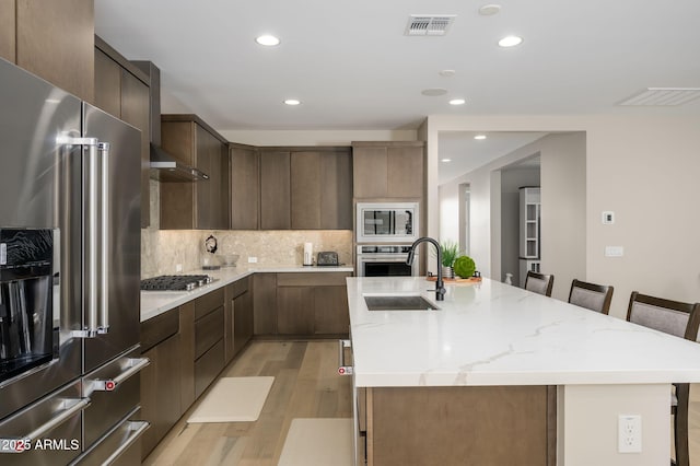 kitchen featuring visible vents, light wood-style floors, a center island with sink, a sink, and appliances with stainless steel finishes