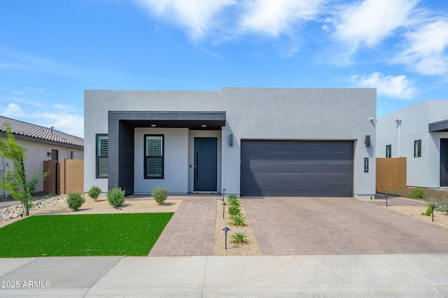 contemporary home featuring a garage, decorative driveway, stucco siding, and fence