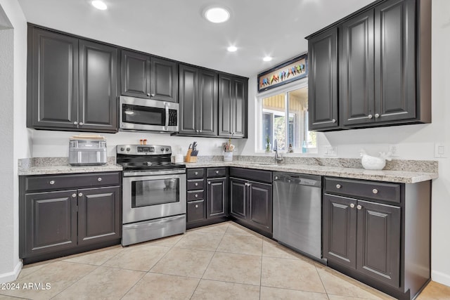 kitchen featuring light stone countertops, sink, stainless steel appliances, and light tile patterned flooring