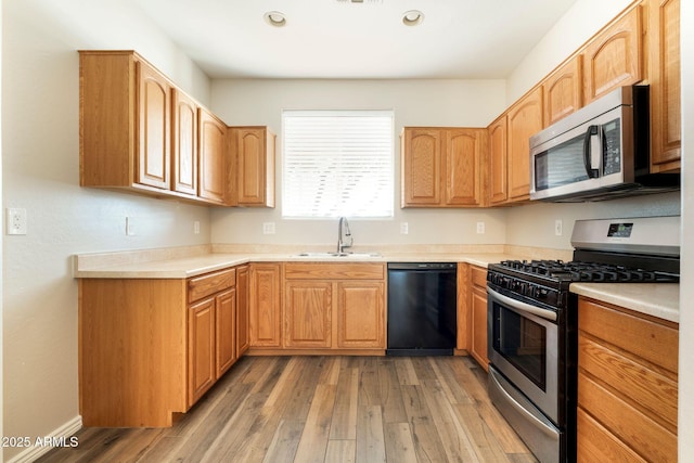 kitchen featuring appliances with stainless steel finishes, light countertops, a sink, and wood finished floors