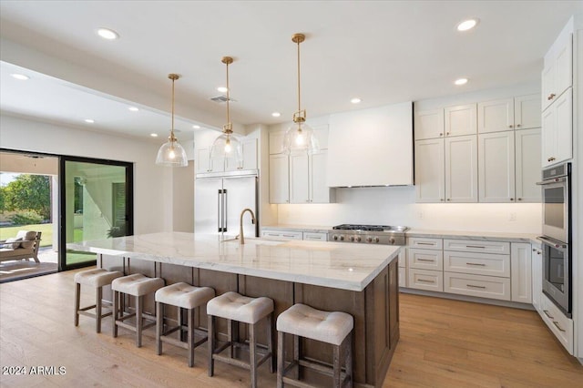 kitchen with appliances with stainless steel finishes, a kitchen island with sink, white cabinets, and light hardwood / wood-style floors