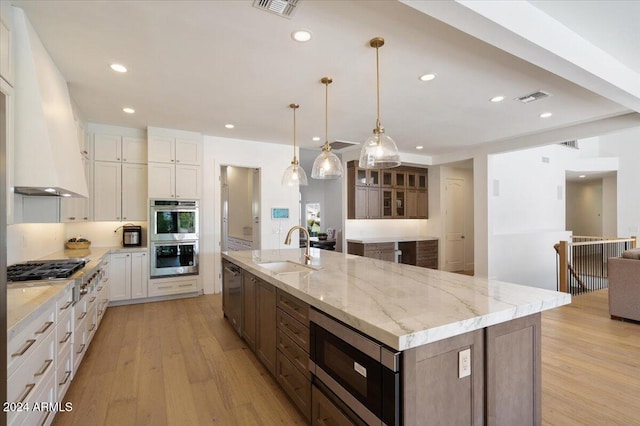 kitchen with a large island with sink, sink, white cabinetry, light hardwood / wood-style floors, and stainless steel appliances