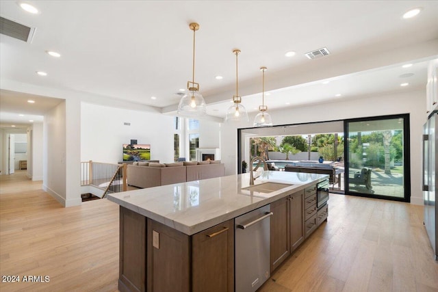 kitchen featuring hanging light fixtures, a center island with sink, light stone counters, light hardwood / wood-style flooring, and sink