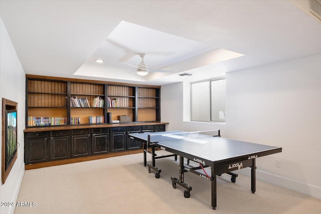 rec room with ceiling fan, light colored carpet, and a raised ceiling