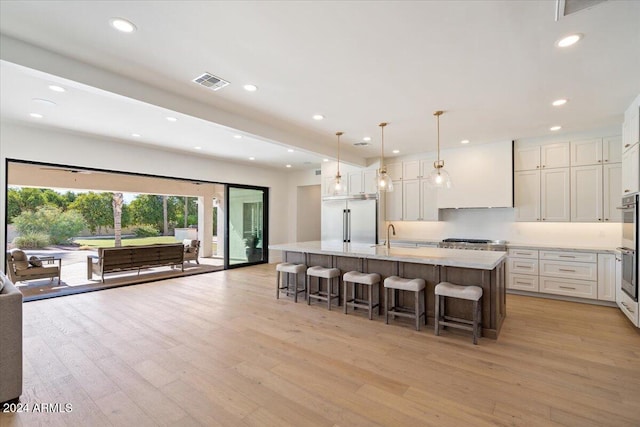 kitchen featuring an island with sink, hanging light fixtures, stainless steel appliances, a kitchen bar, and light hardwood / wood-style floors