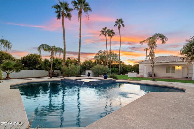 pool at dusk with a patio and an in ground hot tub