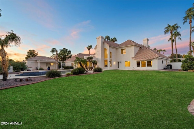 back house at dusk featuring a lawn and central AC unit