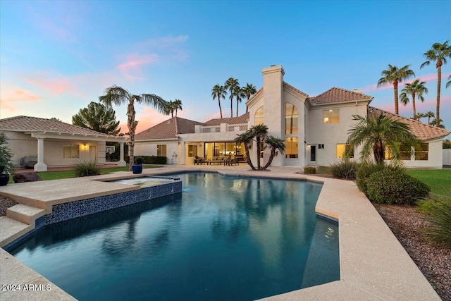 pool at dusk featuring a patio and an in ground hot tub