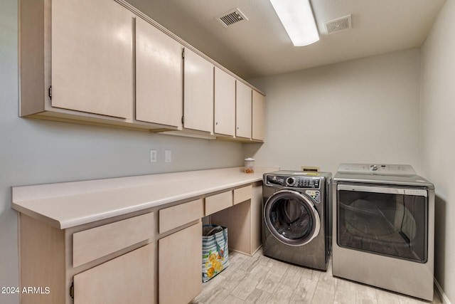 clothes washing area with cabinets, light wood-type flooring, and washer and dryer