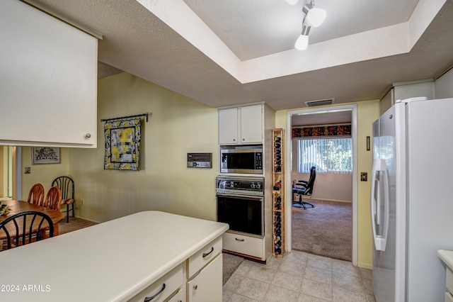 kitchen featuring white refrigerator, black oven, stainless steel microwave, track lighting, and white cabinets