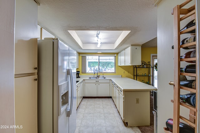 kitchen featuring stainless steel fridge with ice dispenser, a tray ceiling, white cabinetry, sink, and a textured ceiling