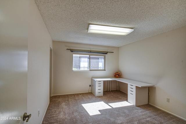 unfurnished office featuring light carpet, built in desk, and a textured ceiling