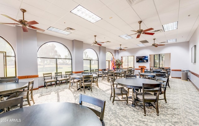 carpeted dining room with ceiling fan and a paneled ceiling