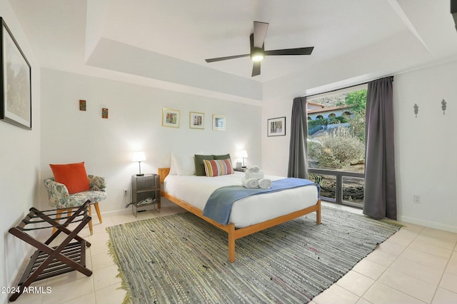 bedroom featuring ceiling fan, light tile patterned flooring, access to exterior, and a tray ceiling