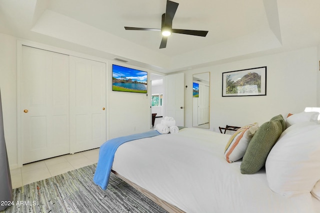 tiled bedroom with a tray ceiling, ceiling fan, and a closet