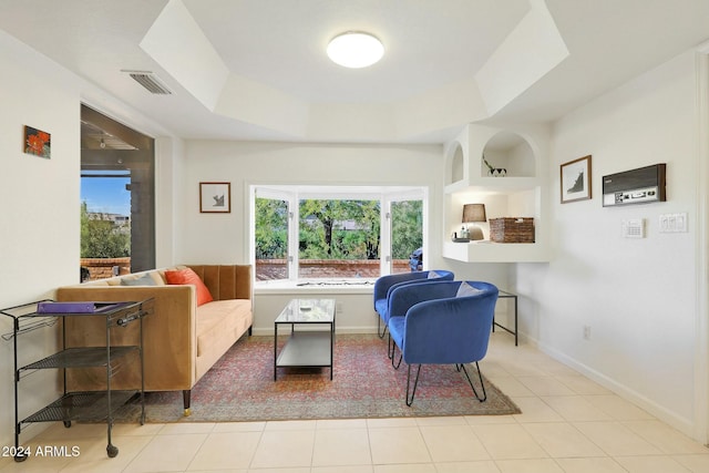 living room featuring a tray ceiling, built in shelves, plenty of natural light, and light tile patterned floors