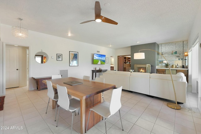 dining area featuring ceiling fan, a large fireplace, light tile patterned floors, and a textured ceiling