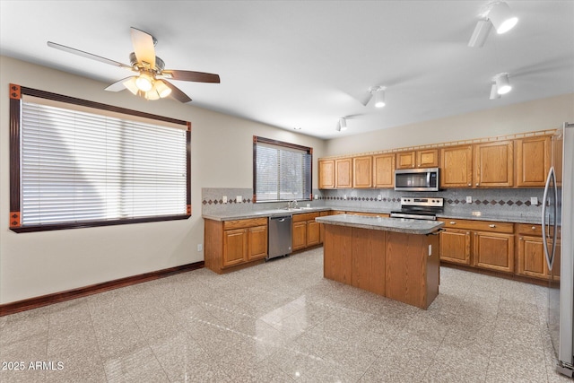 kitchen featuring stainless steel appliances, a center island, baseboards, backsplash, and brown cabinets