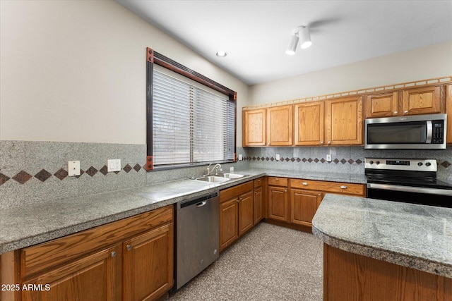 kitchen with appliances with stainless steel finishes, decorative backsplash, a sink, and brown cabinets