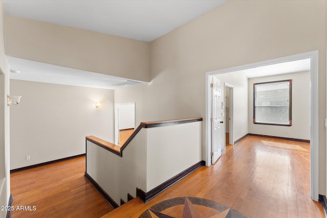 hall featuring light wood-style floors, baseboards, and an upstairs landing