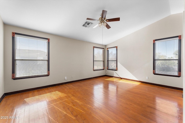 empty room with plenty of natural light, visible vents, vaulted ceiling, and hardwood / wood-style floors