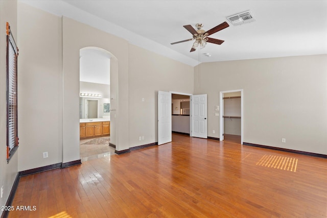 interior space with arched walkways, lofted ceiling, visible vents, ceiling fan, and hardwood / wood-style flooring